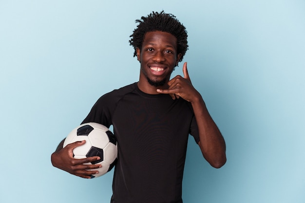 Junger afroamerikanischer Mann, der Fußball spielt, isoliert auf blauem Hintergrund, der eine Handy-Anruf-Geste mit den Fingern zeigt.