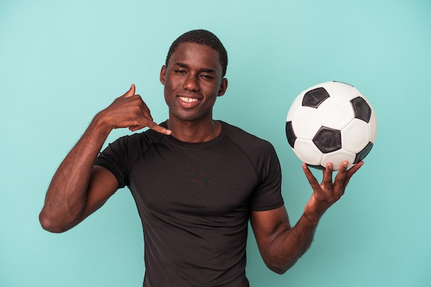 Junger afroamerikanischer Mann, der Fußball spielt, isoliert auf blauem Hintergrund, der eine Handy-Anruf-Geste mit den Fingern zeigt.