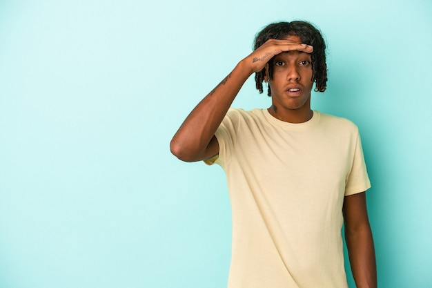Junger afroamerikanischer Mann isoliert auf blauem Hintergrund, der weit weg schaut und die Hand auf die Stirn hält.