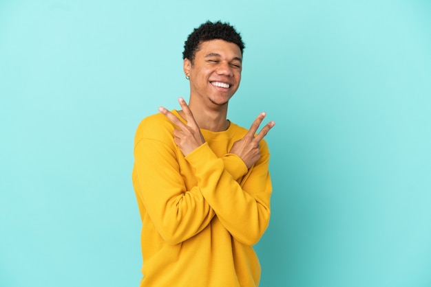 Junger afroamerikanischer Mann isoliert auf blauem Hintergrund lächelt und zeigt Victory-Zeichen