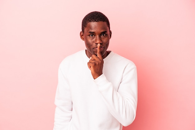 Junger afroamerikanischer Mann isoliert auf rosafarbenem Hintergrund, der ein Geheimnis hält oder um Stille bittet.