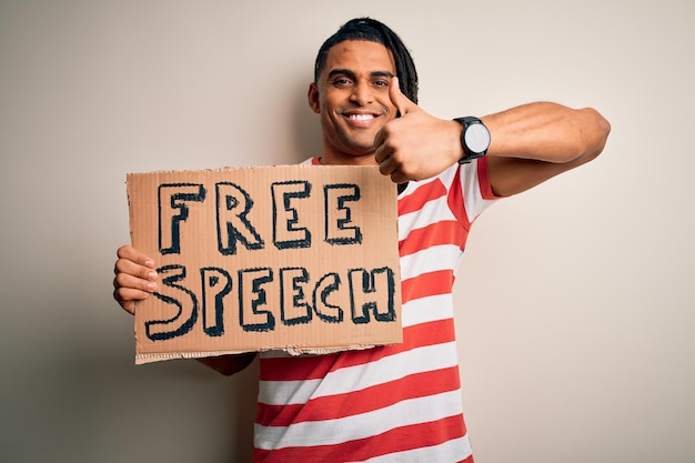 Junger afroamerikanischer Mann mit Dreadlocks, der ein Banner mit der Botschaft zur freien Meinungsäußerung in der Hand hält, protestiert glücklich mit einem breiten Lächeln und macht ein „OK“-Zeichen, den Daumen nach oben mit den Fingern, ein ausgezeichnetes Zeichen