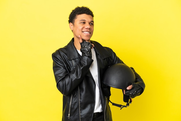 Junger afroamerikanischer Mann mit einem Motorradhelm auf gelbem Hintergrund isoliert, der beim Nachschlagen eine Idee denkt