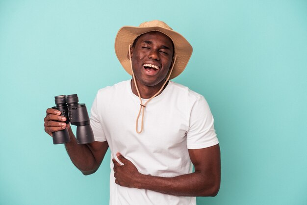 Junger afroamerikanischer Mann mit Fernglas isoliert auf blauem Hintergrund lachen und Spaß haben.