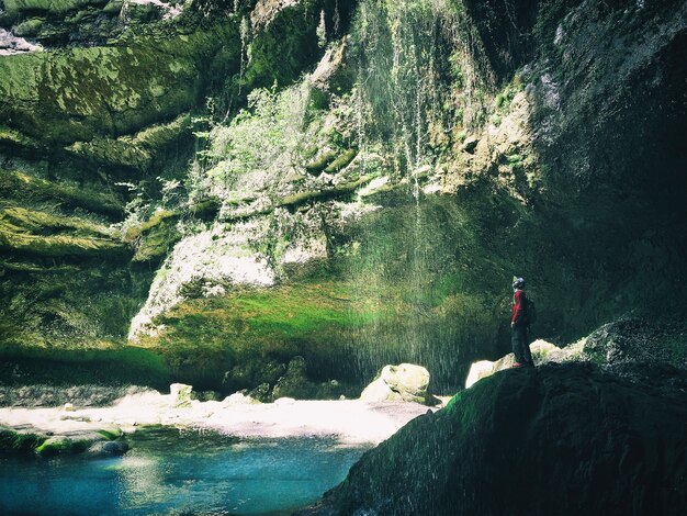 Foto junger aktiver mann, der auf einer klippe steht und auf den wasserfall blickt