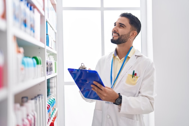 Junger arabischer Apotheker lächelt selbstbewusst und schreibt in die Zwischenablage in der Apotheke