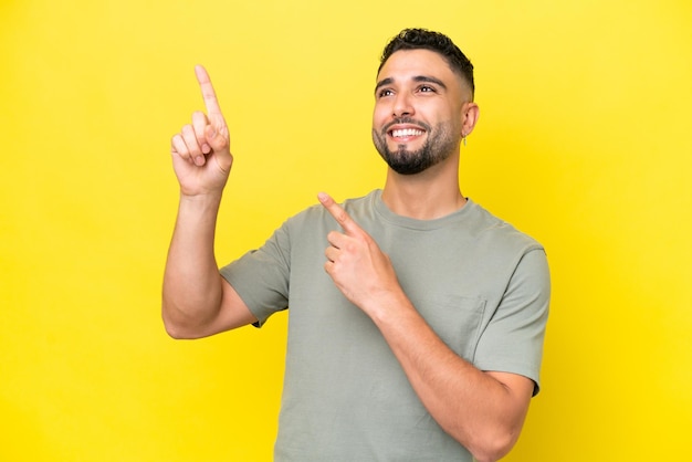 Junger arabischer gutaussehender Mann isoliert auf gelbem Hintergrund, der mit dem Zeigefinger eine großartige Idee zeigt