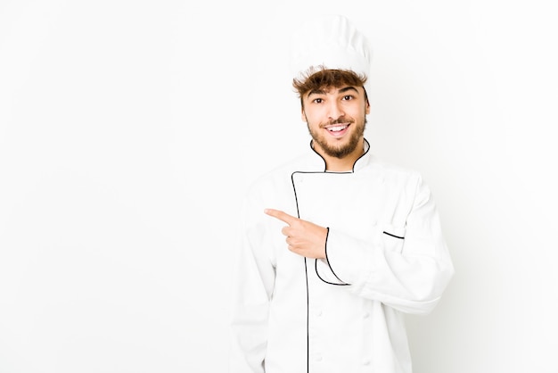 Junger arabischer Kochmann, der lächelt und beiseite zeigt und etwas an der leeren Stelle zeigt.