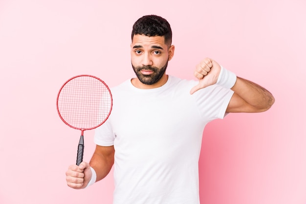 Junger arabischer Mann, der Badminton spielt, zeigt isoliert eine Abneigungsgeste, Daumen nach unten. Uneinigkeit Konzept.