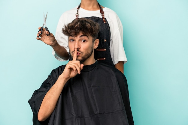 Foto junger arabischer mann, der bereit ist, einen haarschnitt einzeln auf blauem hintergrund zu bekommen, der ein geheimnis hält oder um stille bittet.