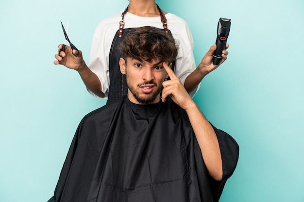 Foto junger arabischer mann, der bereit ist, einen haarschnitt einzeln auf blauem hintergrund zu bekommen, der eine enttäuschungsgeste mit dem zeigefinger zeigt.
