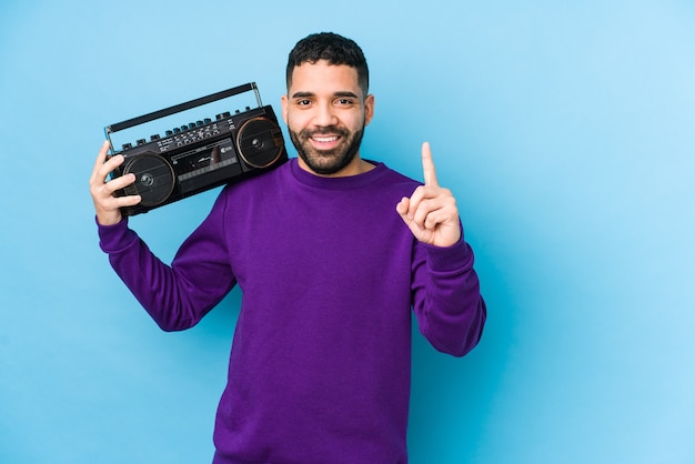 Junger arabischer Mann, der eine Radio-Kassette isoliert hält Junger arabischer Mann, der Musik hört, die Nummer eins mit Finger zeigt.