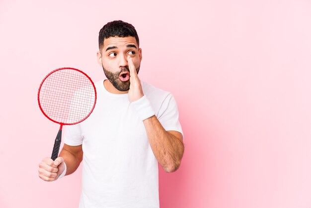 Junger arabischer Mann, der isoliert Badminton spielt, sagt eine geheime heiße Bremsnachricht und schaut zur Seite