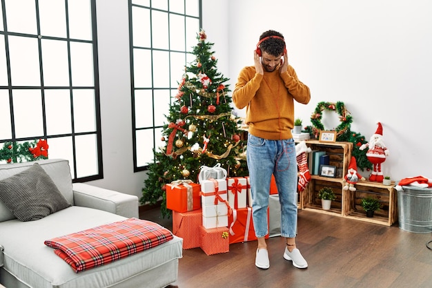 Junger arabischer mann, der musik hört und tanzt, der zu hause am weihnachtsbaum steht.