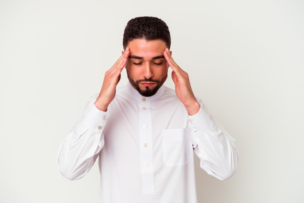 Junger arabischer Mann, der typische arabische Kleidung trägt, die auf weißen berührenden Schläfen isoliert ist und Kopfschmerzen hat.