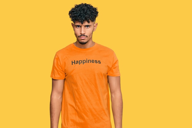 Junger arabischer Mann trägt T-Shirt mit Glückswortbotschaft, skeptisch und nervös, runzelt die Stirn, verärgert wegen der problematischen negativen Person