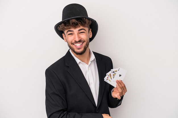 Junger arabischer Zauberermann, der magische Karten lokalisiert auf weißem Hintergrund hält, lacht und Spaß hat.