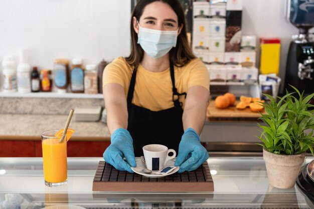 Junger Arbeiter, der Tasse Kaffee innerhalb des Restaurants beim Tragen der Gesichtsschutzmaske gibt