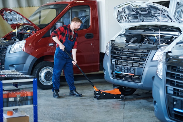 Foto junger arbeiter des reparaturdienstzentrums, der wagen vor der technischen überprüfung unter auto setzt