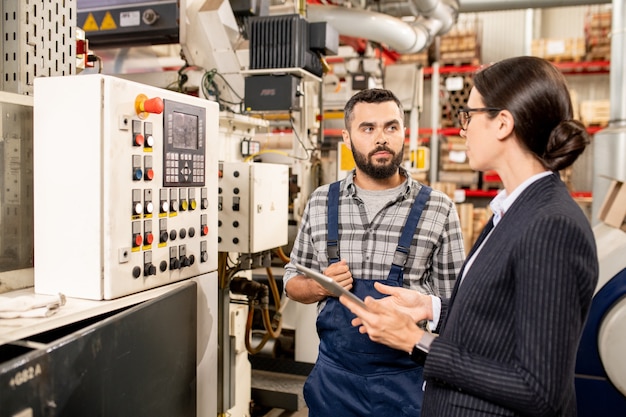 Junger Arbeiter einer zeitgenössischen Fabrik berät seinen Partner über neue Methoden der Rohstoffverarbeitung