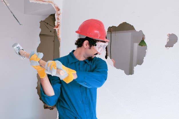 junger Arbeiter mit einem roten Schutzhelm und trägt einen blauen Kesselanzug. Abbruchkonzept