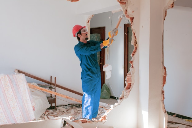 junger Arbeiter mit einem roten Schutzhelm und trägt einen blauen Kesselanzug. Abbruchkonzept