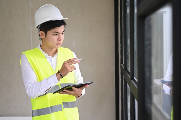 Junger Architekt mit Helm und Tablette auf der Baustelle, Checklistenkonzept