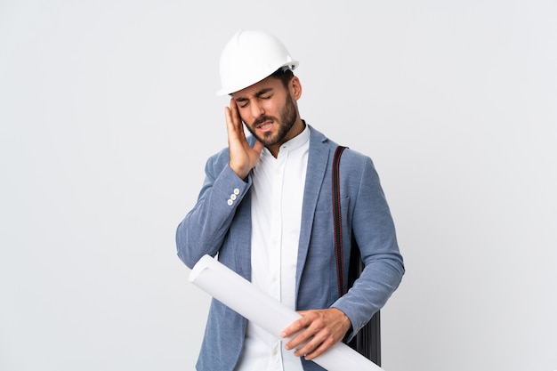 Junger Architektenmann mit Helm und Halteplänen lokalisiert auf weißer Wand mit Kopfschmerzen