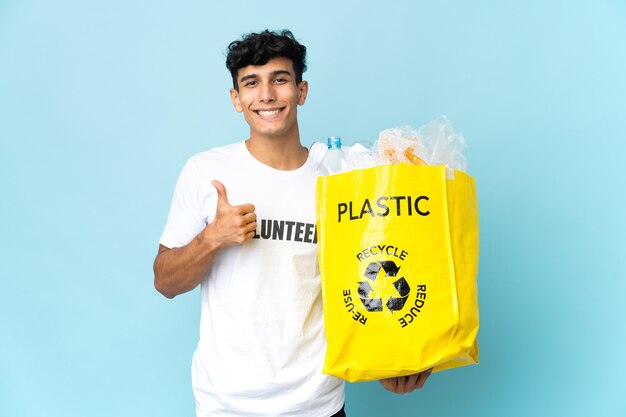 Junger argentinischer Mann, der eine Tasche voll Plastik hält und eine Daumen hoch Geste gibt