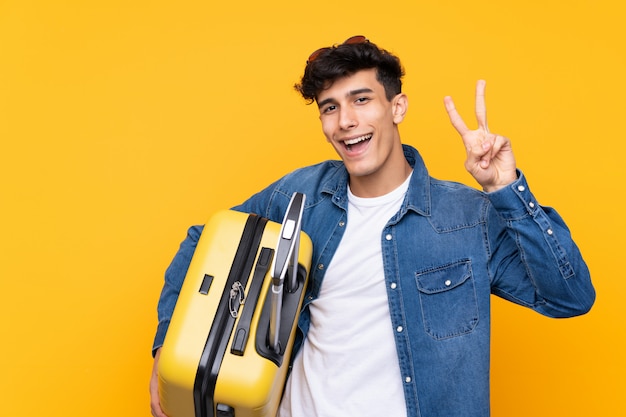 Junger argentinischer Mann in den Ferien mit Reisekoffer und Sieggeste machend
