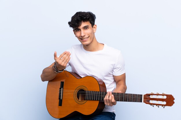 Junger argentinischer Mann mit der Gitarre, die einlädt, mit der Hand zu kommen. Schön, dass Sie gekommen sind