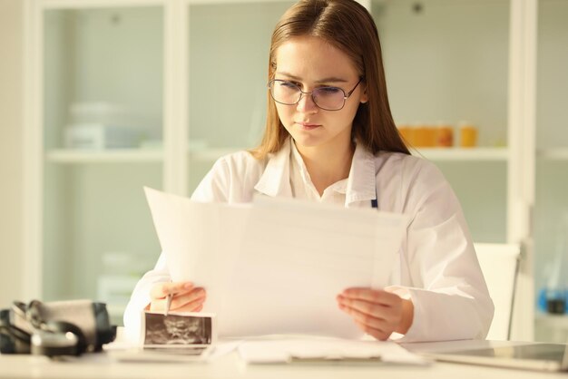 Junger Arzt mit Brille liest medizinische Dokumente, während er in der medizinischen Klinik am Tisch sitzt