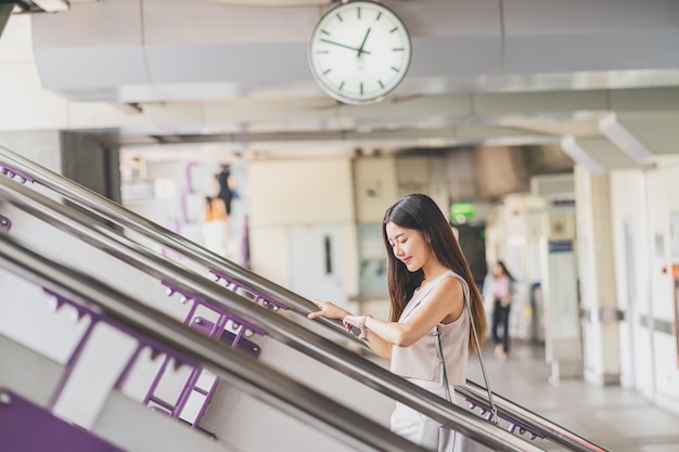 Junger Asiatinpassagier, der intelligenten Handy verwendet und herauf die Treppe in der U-Bahnstation geht