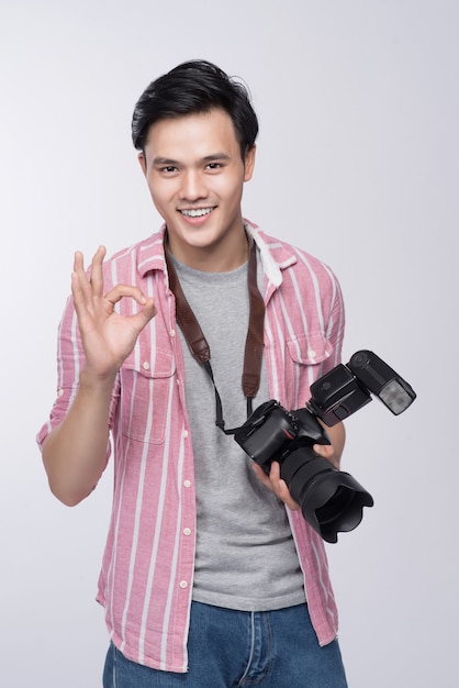 Junger asiatischer Fotograf, der eine Digitalkamera hält, während er im Studio arbeitet