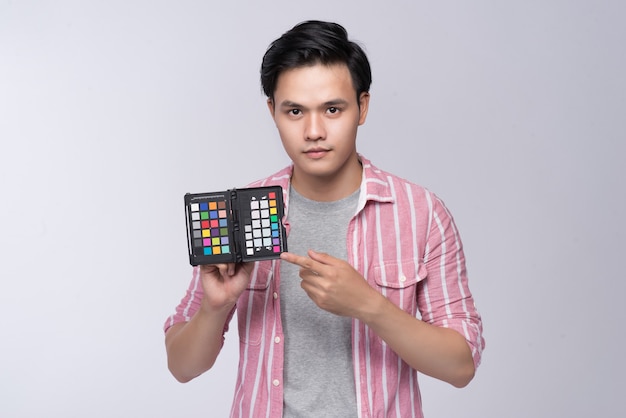Junger asiatischer Fotograf, der eine Farbprüfkarte hält, während er im Studio arbeitet