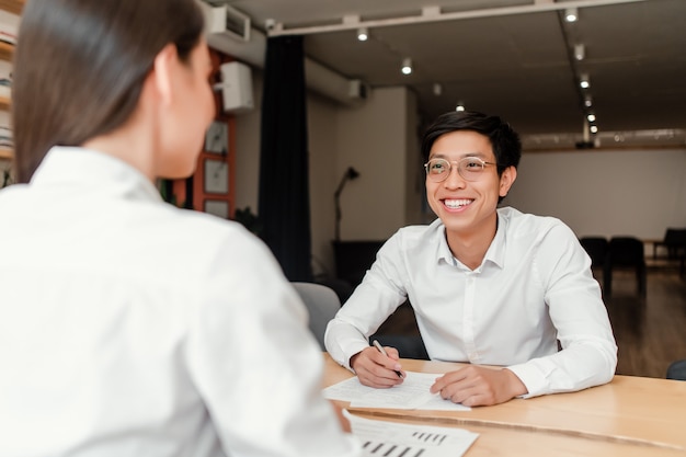 Junger asiatischer Geschäftsmann auf dem Vorstellungsgespräch mit einer Frau im Büro