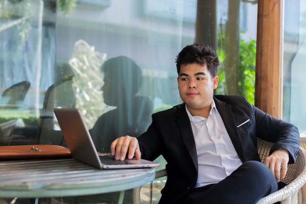 Junger asiatischer Geschäftsmann, der an seinem Laptop Szene in der im Freien arbeitet