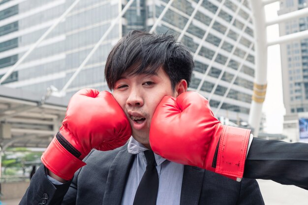 Junger asiatischer Geschäftsmann, der in der Stadt mit rotem Boxhandschuh Schlag bekommt