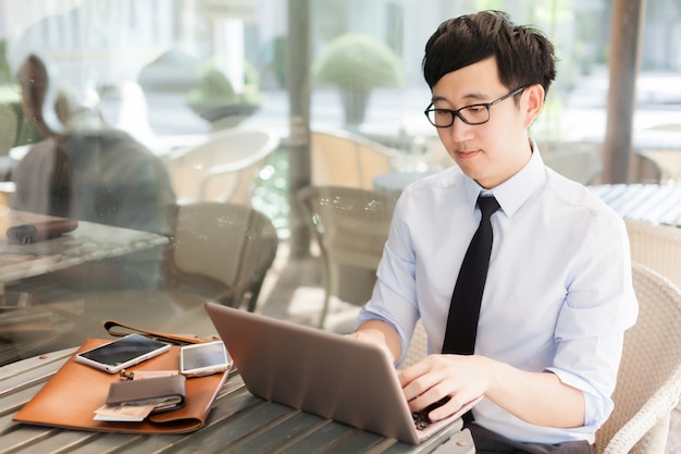 Junger asiatischer Geschäftsmann, der mit seinem Laptop Szene in der im Freien arbeitet