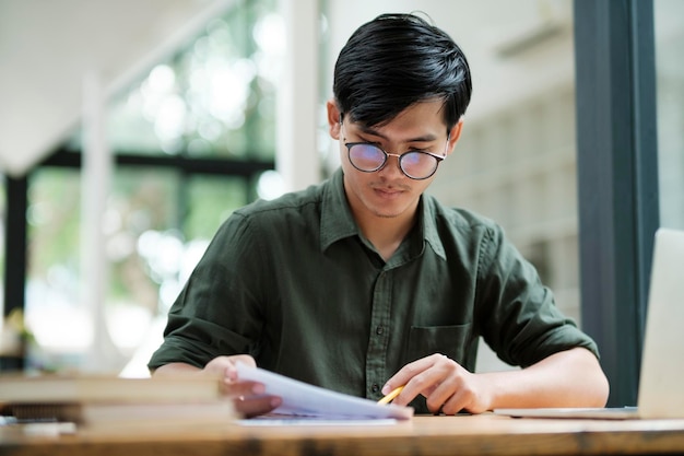 Junger asiatischer Geschäftsmann oder Student, der online am Computer-Laptop arbeitet