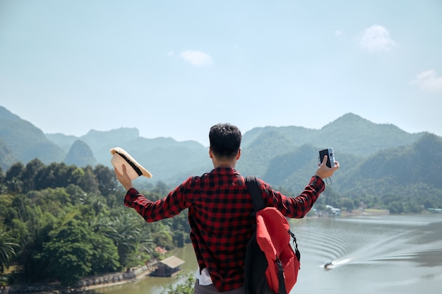 Junger asiatischer Hipster-Mann, der mit einem Rucksack im Sommerwaldreise-Reiselebensstilkonzept reist