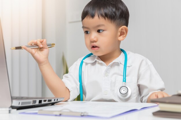 Junger asiatischer Junge, der Doktor und Behälter beim Betrachten auf Computerlaptop spielt.