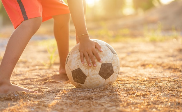 Junger asiatischer Junge, der morgens mit altem und schmutzigem klassischem Fußball spielt