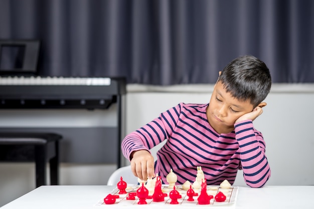 Junger asiatischer Junge, der Schach im Raum spielt