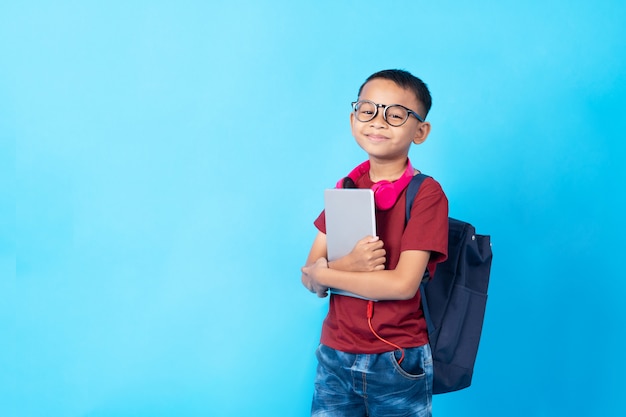 Junger asiatischer Jungenstudent, thailändisches Kind, das Tablette und Schultasche hält