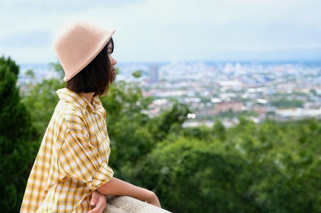 Junger asiatischer Mädchenreisender, der im Stadt- und draußen Naturansichthintergrund steht