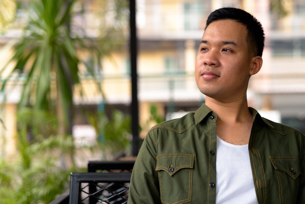 Junger asiatischer Mann, der am Kaffeehaus denkt und sich entspannt