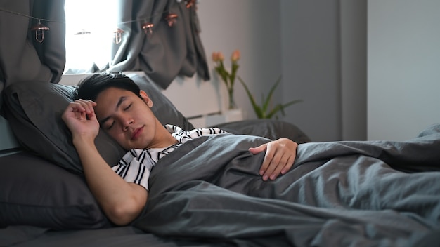 Junger asiatischer Mann, der am Wochenende in seinem bequemen Bett schläft.