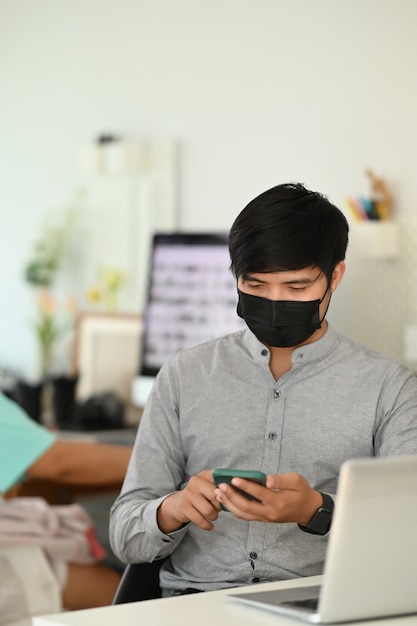 Junger asiatischer Mann, der an einem Laptop an seinem Schreibtisch arbeitet