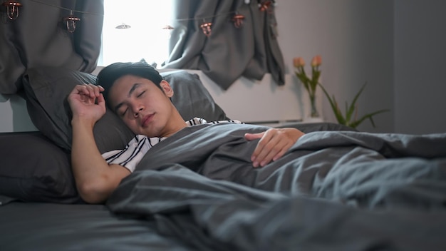 Junger asiatischer Mann, der auf einem bequemen Bett schläft